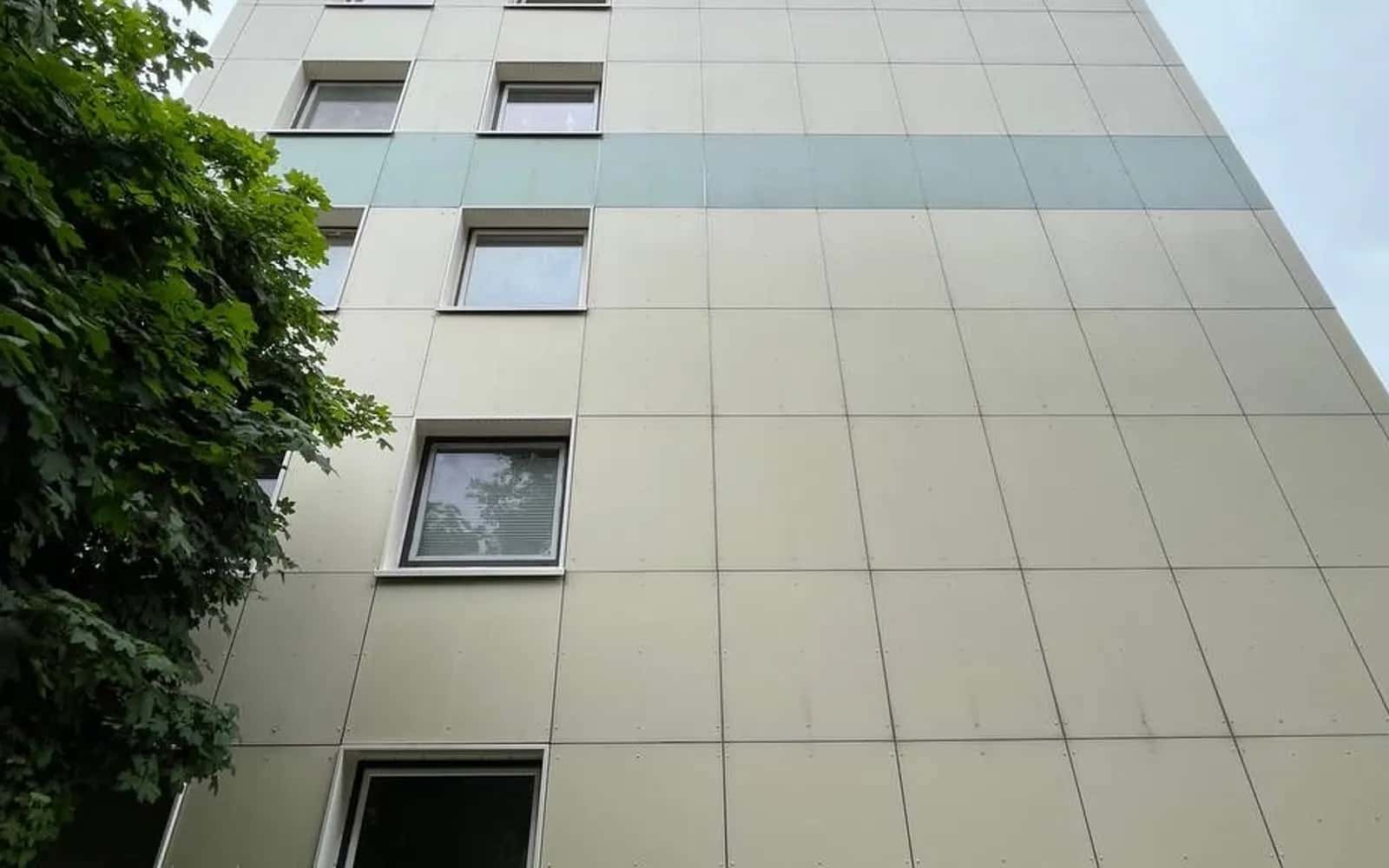 Fassade eines hellen Wohnhochhauses mit Fensterreihen, von unten gesehen
