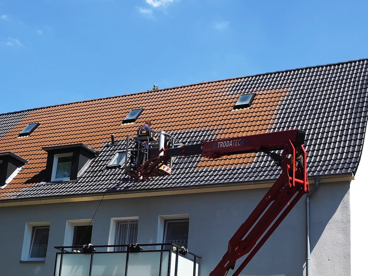 Mitarbeiter reinigt vom Korb der Arbeitsbühne aus ein Ziegeldach