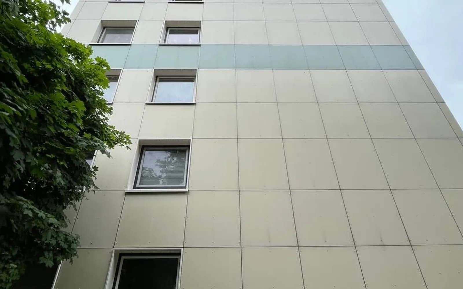 Fassade eines hellen Wohnhochhauses mit Fensterreihen, von unten gesehen