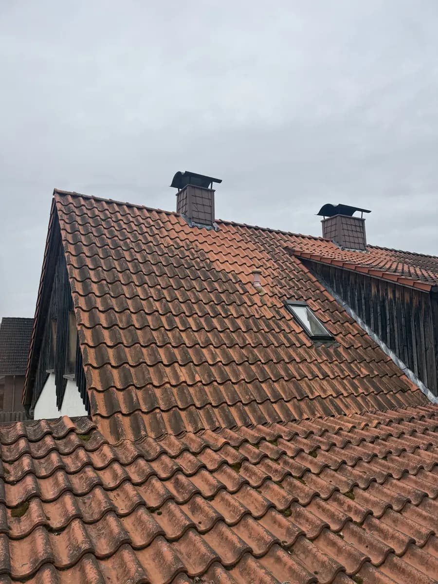 Rotes Pfannendach mit dunklen Verschmutzungsschleiern unter bedecktem Himmel