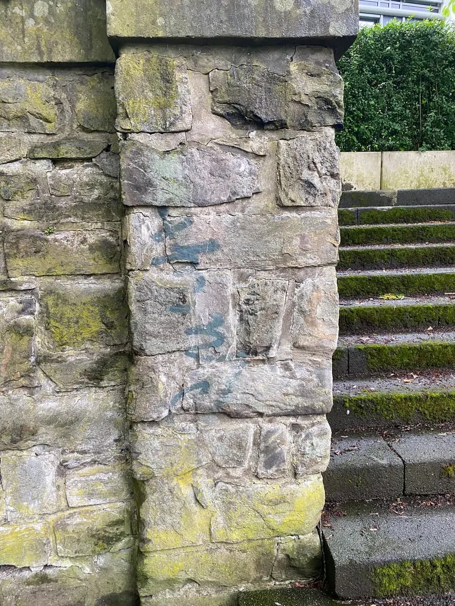 Natursteinpfeiler einer Treppenanlage mit blauem Graffiti-Tag
