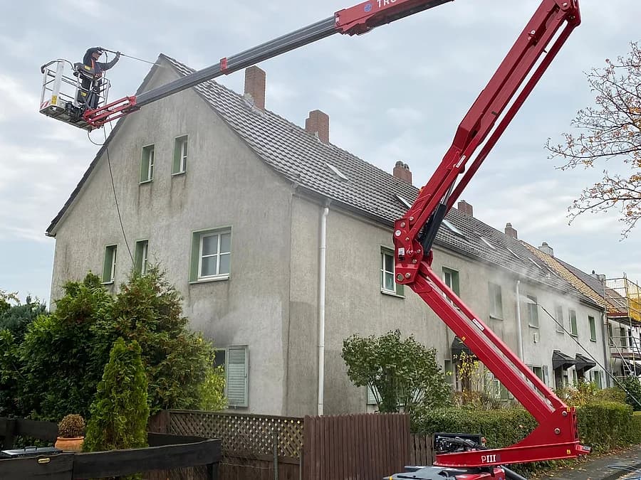 Rote Arbeitsbühne im Einsatz vor einer Häuserzeile