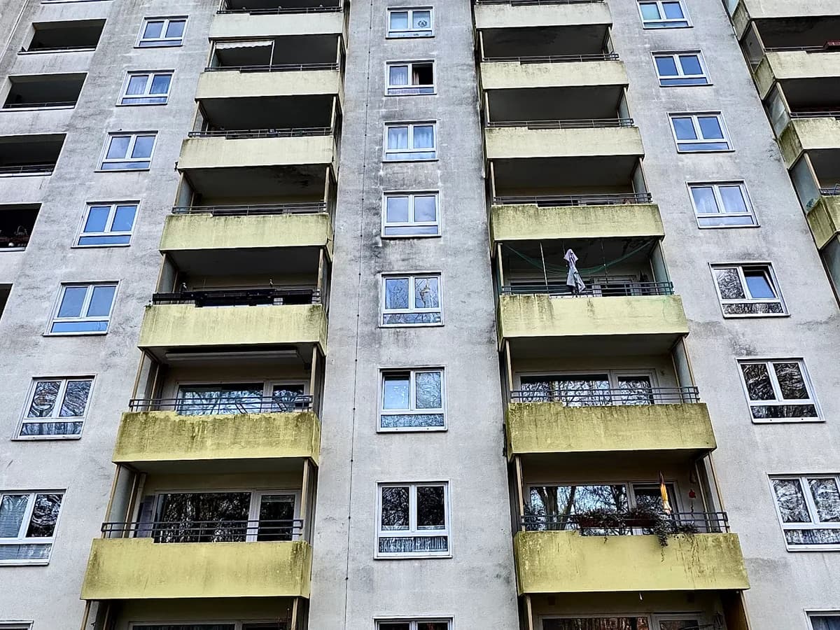 Hochhausfassade mit stark veralgten, gräulich-grünen Balkonbrüstungen vor der Reinigung