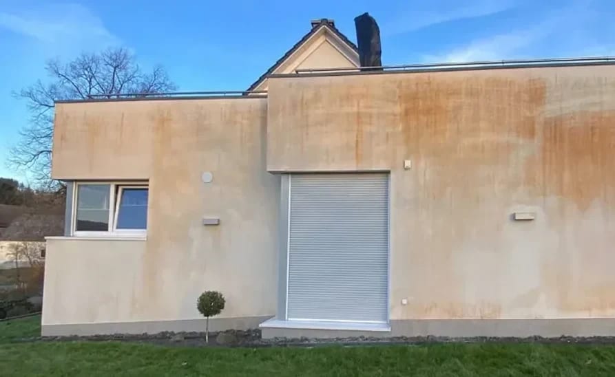Wohnhaus mit hellem Putz, dessen Wetterseite flächig gelbbraun verfärbt ist, vor der Fassadenreinigung