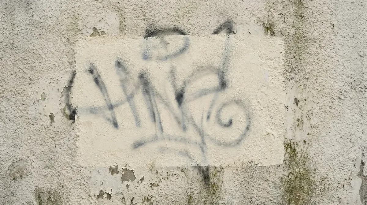 Überstrichenes Graffiti auf einer Putzwand: heller Farbfleck, durch den die alten Sprühlinien wieder durchschlagen