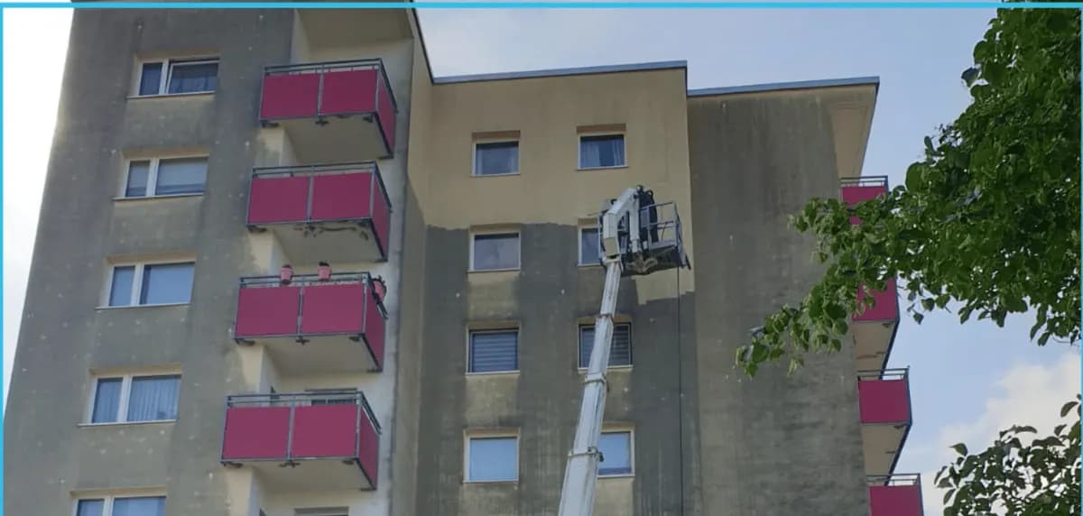 Hochhausfassade während der Reinigung: oberhalb der Hebebühne heller Putz, darunter noch grau-grüner Belag