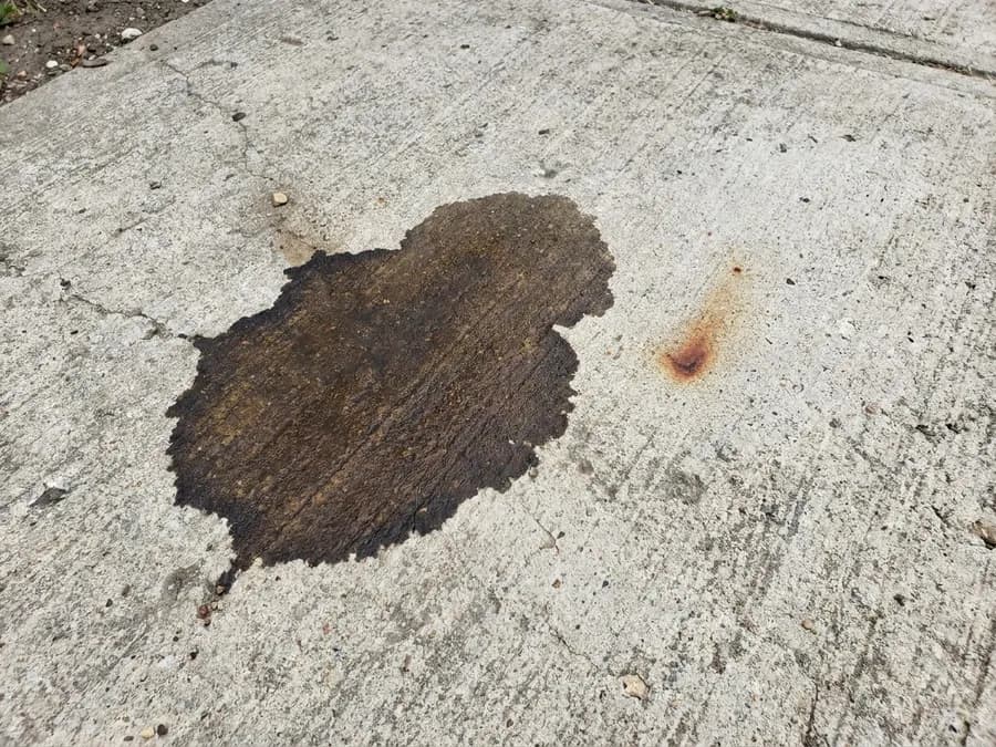 Punktueller dunkler Ölfleck auf einer gepflasterten Stellfläche