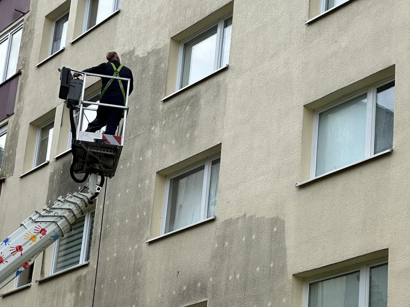 Mitarbeiter im Korb einer Hebebühne an einer Wohnhausfassade, links die gereinigte, rechts die noch verschmutzte Fläche